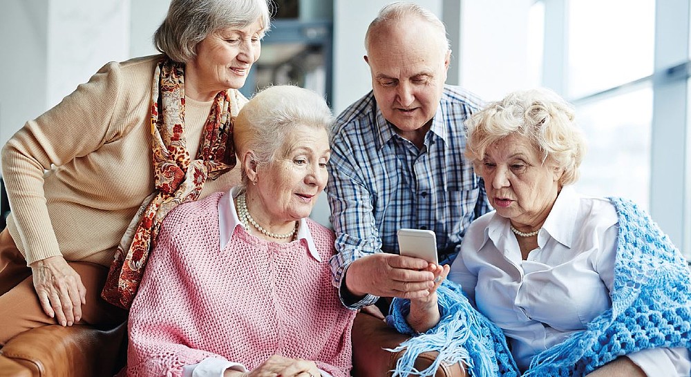 Vier Seniorinnen und ein Senior sitzen zusammen und schauen auf ein Handydisplay