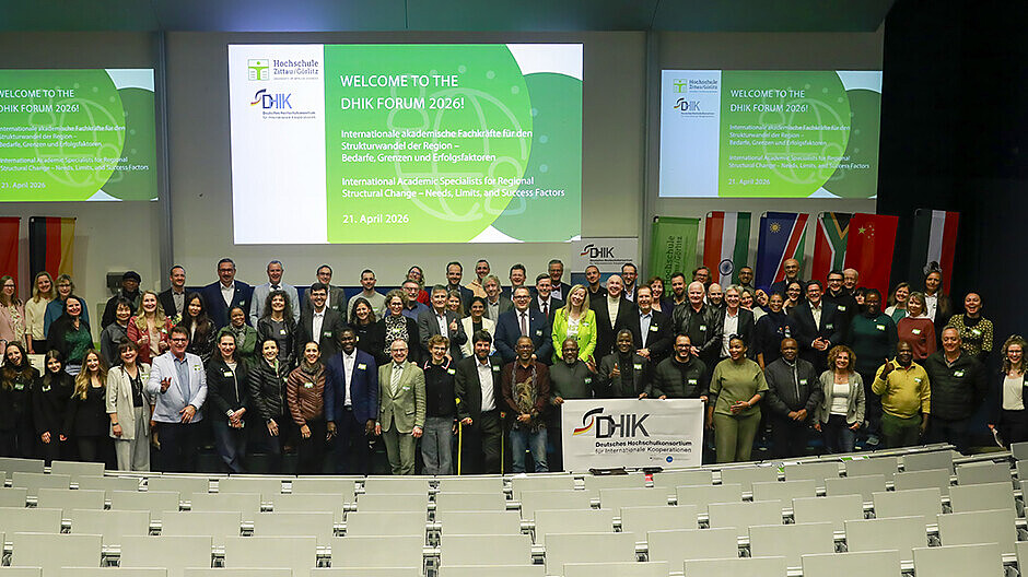 Teilnehmende des Forums des Deutschen Hochschulkonsortiums für Internationale Kooperationen stehen zum Gruppenbild nebeneinander im Audimax vor den Sitzreihen.