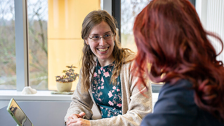 Claudia Döring berät eine rothaarige Frau an einem Tisch sitzend mit aufgeklappten Laptop.