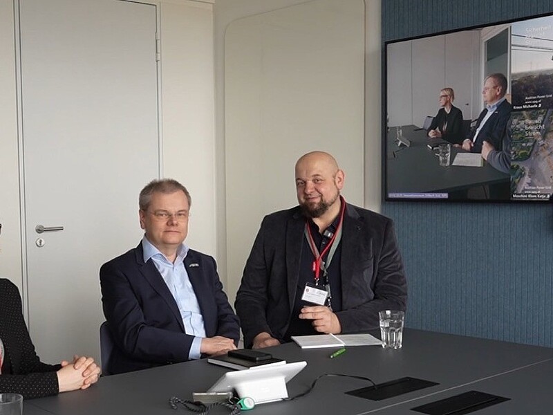3 Personen in Präzenz am Tisch in einer Videokonferenz