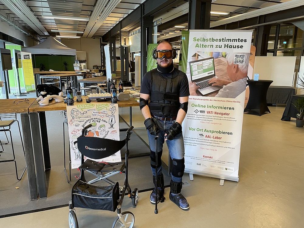 Mann in einem Altersanzug steht vor einem Messestand