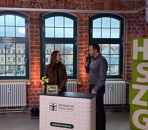 Die Moderatorin im Gespräch mit einem Gast hinter der Messetheke im TV-Studio.