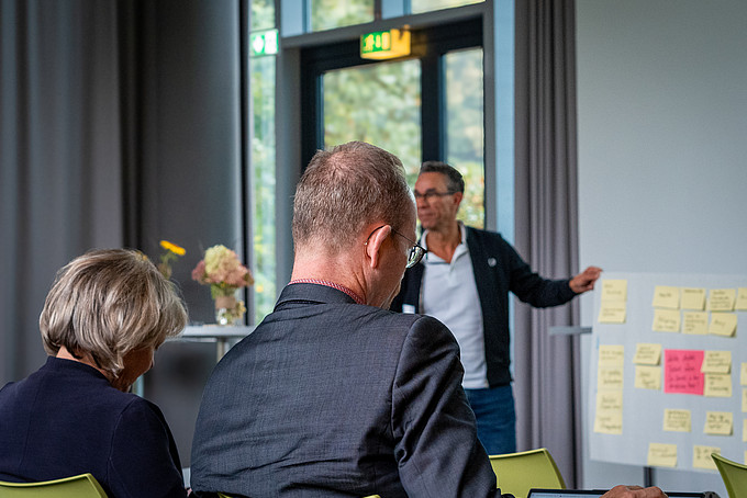 Herr Tschentscher von der AWO Oberlausitz präsentiert die Ergebnisse seines Workshops an einem Flipchart. Im Vordergrund sind zwei Teilnehmende zu sehen.