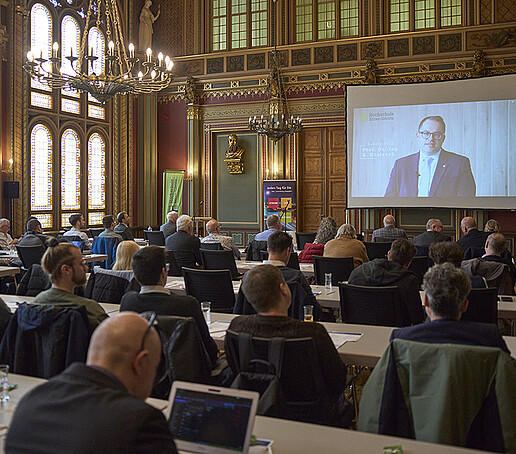 Über eine Leinwand richtet der Rektor seine digitalen Grußworte an das Publikum.