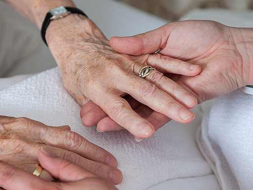 Zwei Hände einer deutlich älteren Person halten die Hände einer jüngeren Person.