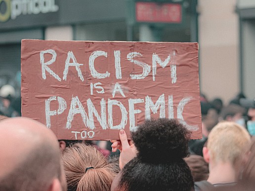 Demonstrierende gegen Alltagsrassismus halten ein Schild mit der Aufschrift "Rassismus ist auch eine Pandemie" in die Höhe.