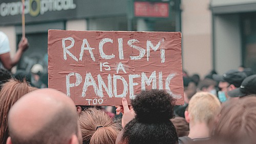 Demonstrierende gegen Alltagsrassismus halten ein Schild mit der Aufschrift "Rassismus ist auch eine Pandemie" in die Höhe.