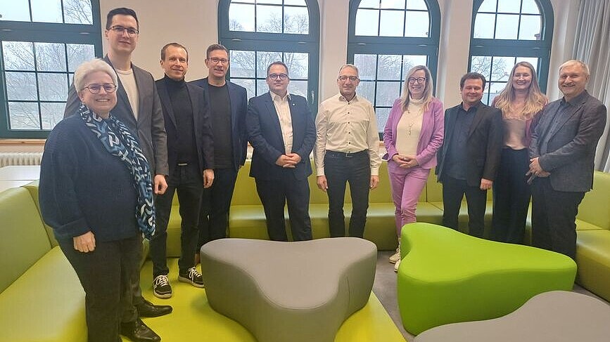 Vertretende der HSZG und Fraunhofer ENAS stehen zwischen grünen Möbeln zum Gruppenbild und lächeln in die Kamera.