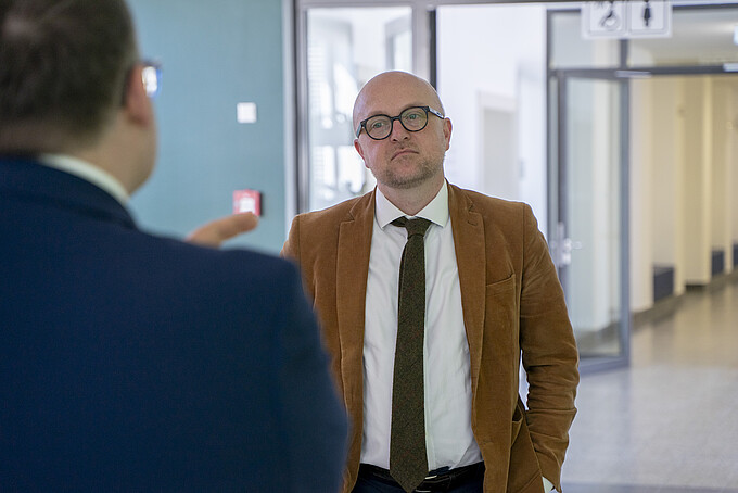 Herr Denk steht im Flur von Haus eins und hört dem Rektor zu, der vor ihm steht.