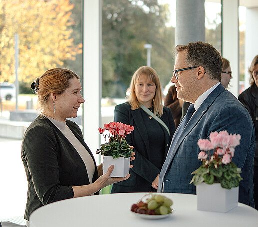 Eine Professorin hält ein Blumengesteck in den Händen und unterhält sich mit dem Rektor.