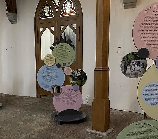 In einer Kirche sind rund ausgeschnittene Ausstellungsstücke zu sehen. Eine Kirchentür im Hintergrund.