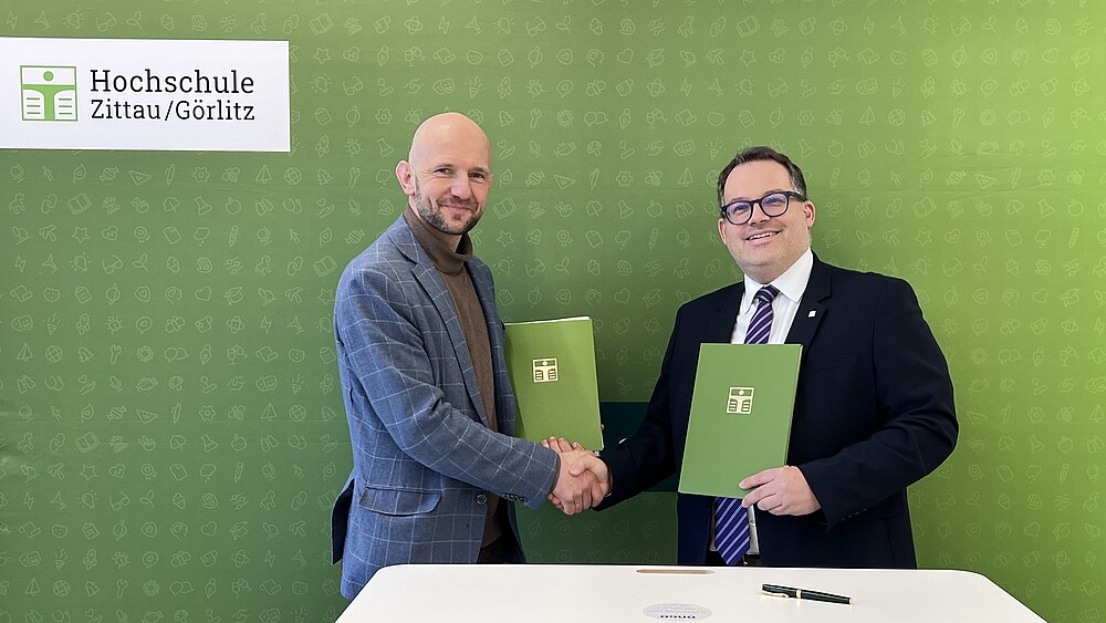 Landrat Dr. Stephan Meyer und Rektor Prof. Dr.-Ing. Alexander Kratzsch halten nach der Vertragsunterzeichnung die unterzeichneten Kooperationsvereinbarungen in den Händen.