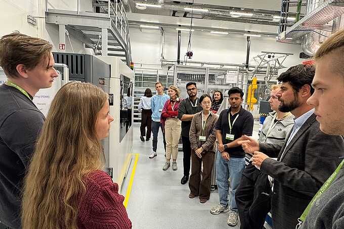 Im Technikum steht Prof. Scholz mit einer Gruppe vor einer Maschine und erklärt deren Funktion.